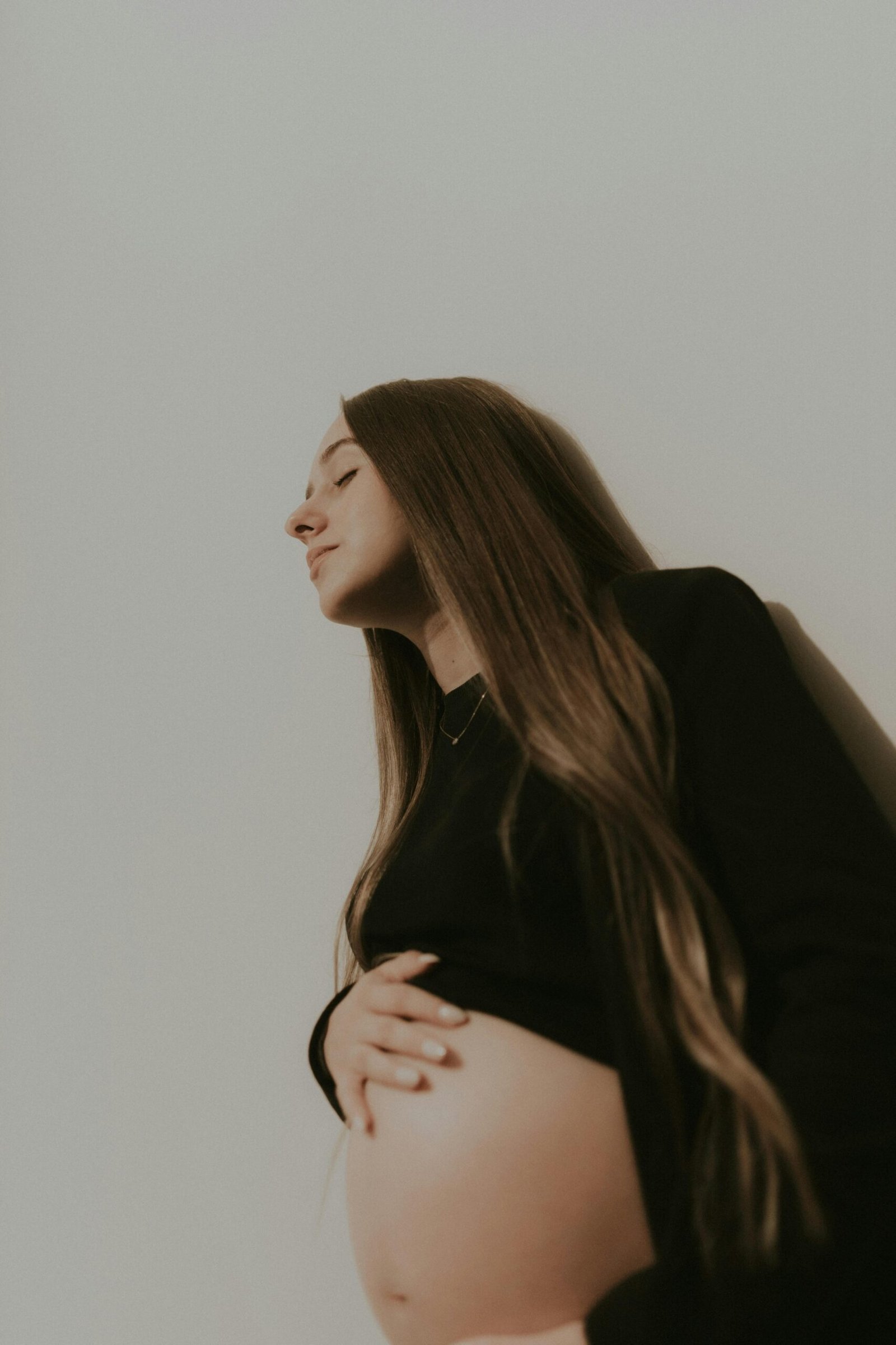 A serene portrait of a pregnant woman with eyes closed, captured in a studio setting.