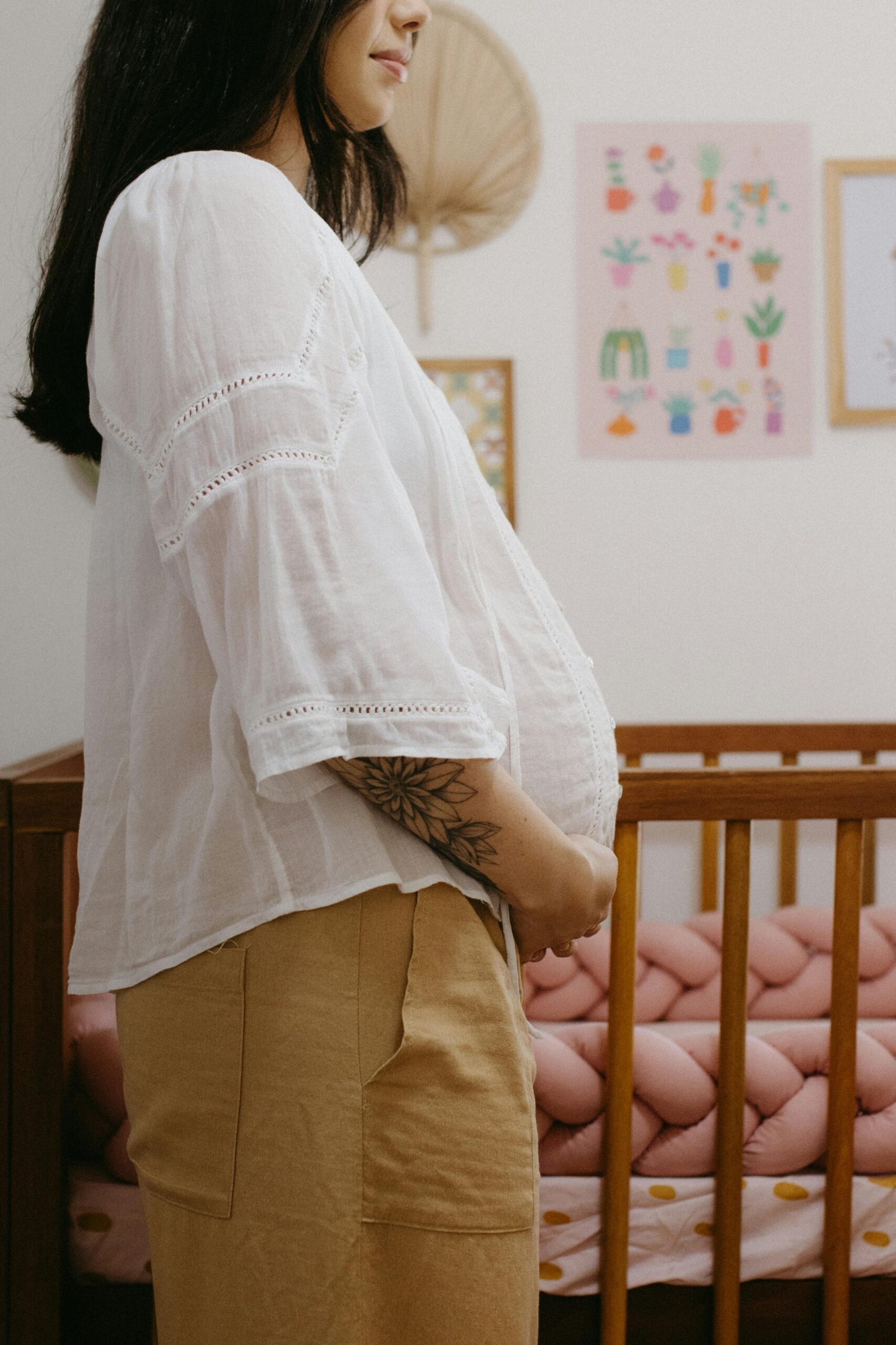 Pregnant woman stands by crib in a warm, decorated nursery, embodying anticipation and maternal warmth.